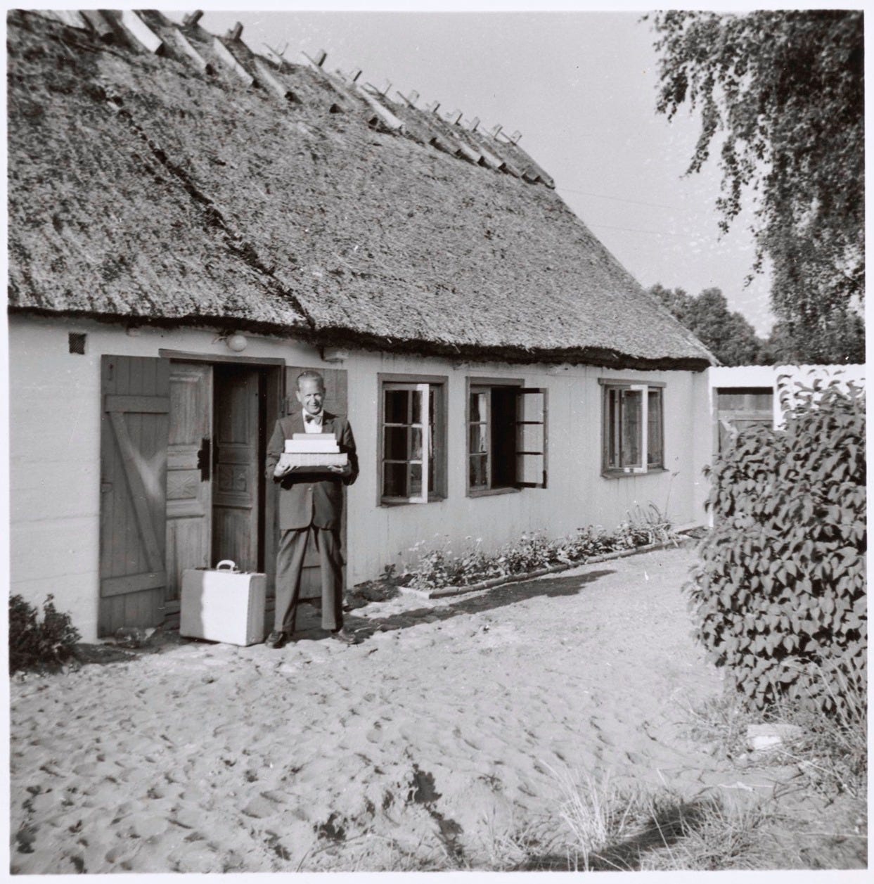 A man with a pile of books in front of a summer cottage