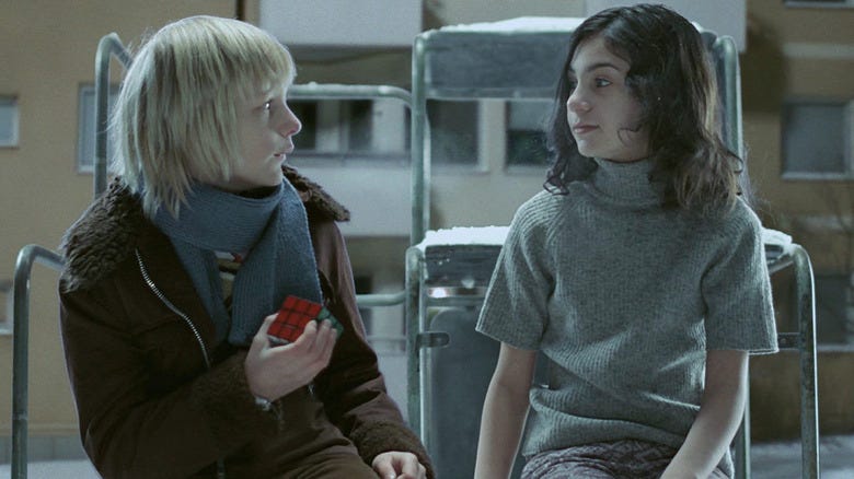 Scene from vampire film Let The Right One In: Oskar, a young blond boy, sits with Eli, a pale child vampire. They look awkwardly at each other.