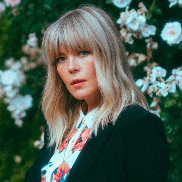 A woman sits in front of a floral background A woman sits in front of a floral background