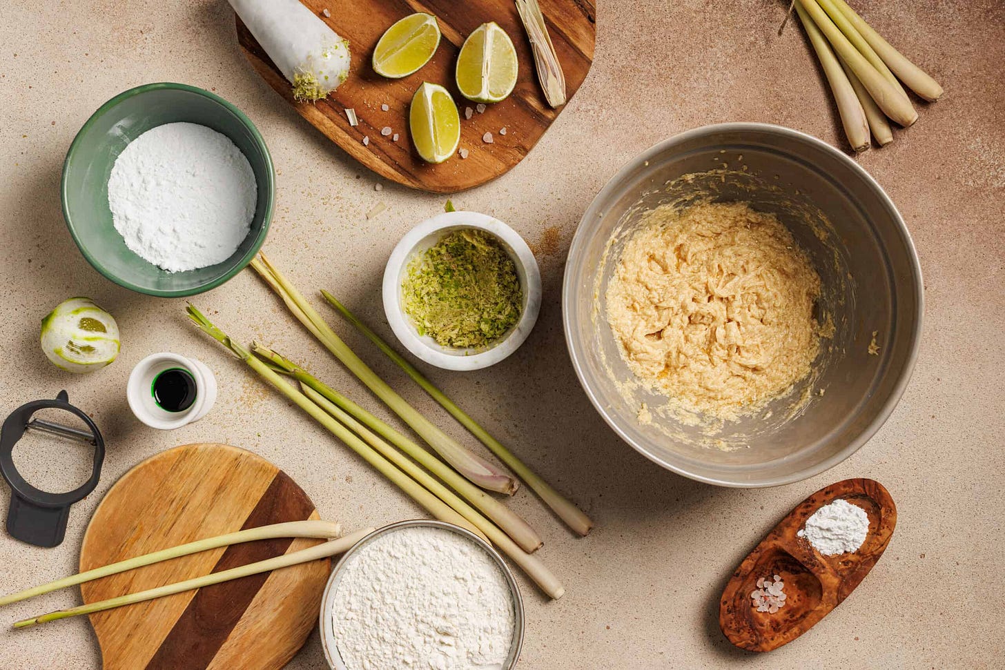 A table full of ingredients for lemongrass cookies. In a bowl there is minced lemongrass into 1/4 cup white sugar to release aromatic oils. 
