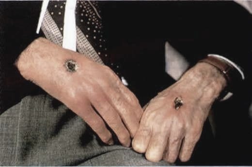 This may contain: a man in a suit and tie holding his hands together with two rings on their fingers