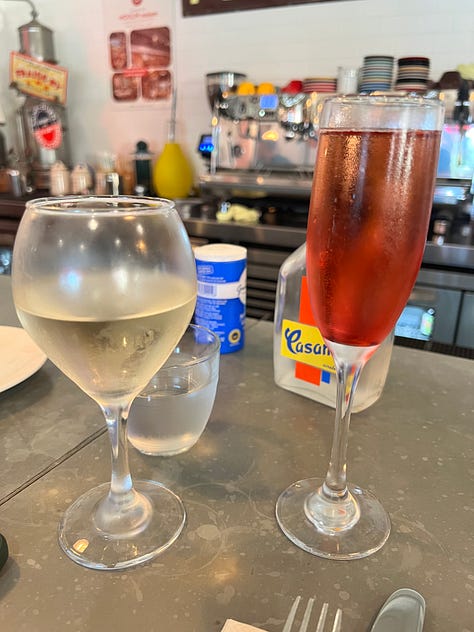 Three photos from Bouillon by Moulin: a glass of white wine and a kir royale on the counter, a decorative tile mural of a woman with a hand mirror, and a vintage Marcadet Poissonniers sign above the bar.