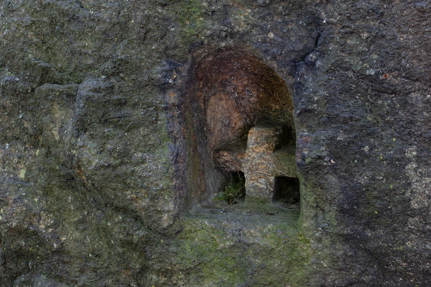 a stout cross in a little arch-shaped depression carved into a dark-colored rock