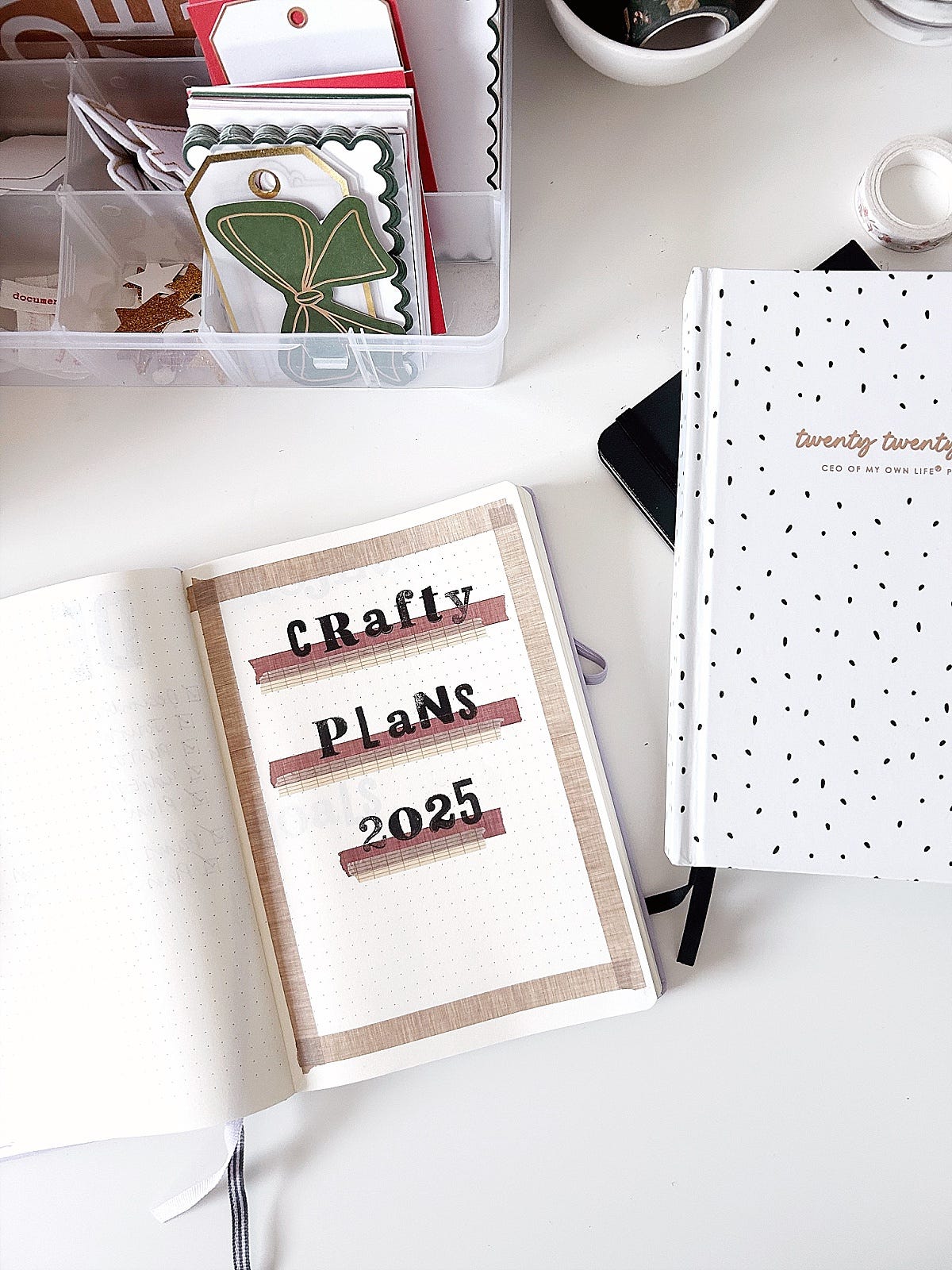 Notebook lying open on desk strewn with scrapbooking supplies. On the page, text reads Crafty Plans 2025.