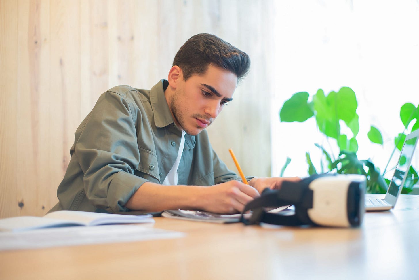 Focused young man working at a desk with a laptop and papers in a sunlit office. Focused young man working at a desk with a laptop and papers in a sunlit office.