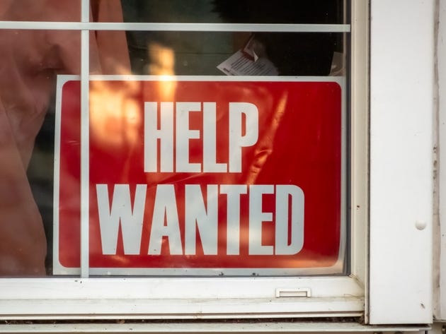 A red HELP WANTED sign displayed prominently in a store window, signaling the business"s need for additional staff.