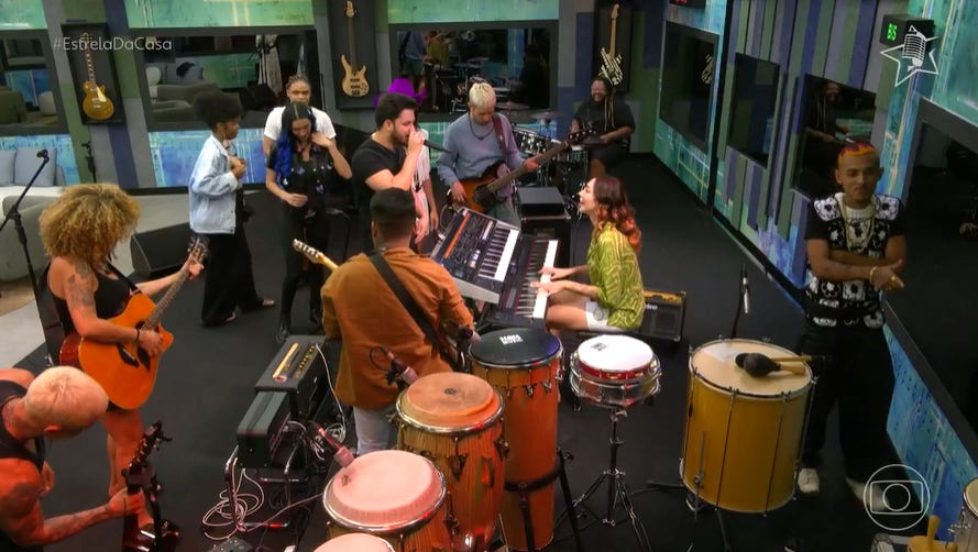 imagem do programa Estrela da Casa. 14 pessoas estão ao redor de instrumentos musicais, algumas tocando, algumas simplesmente olhando