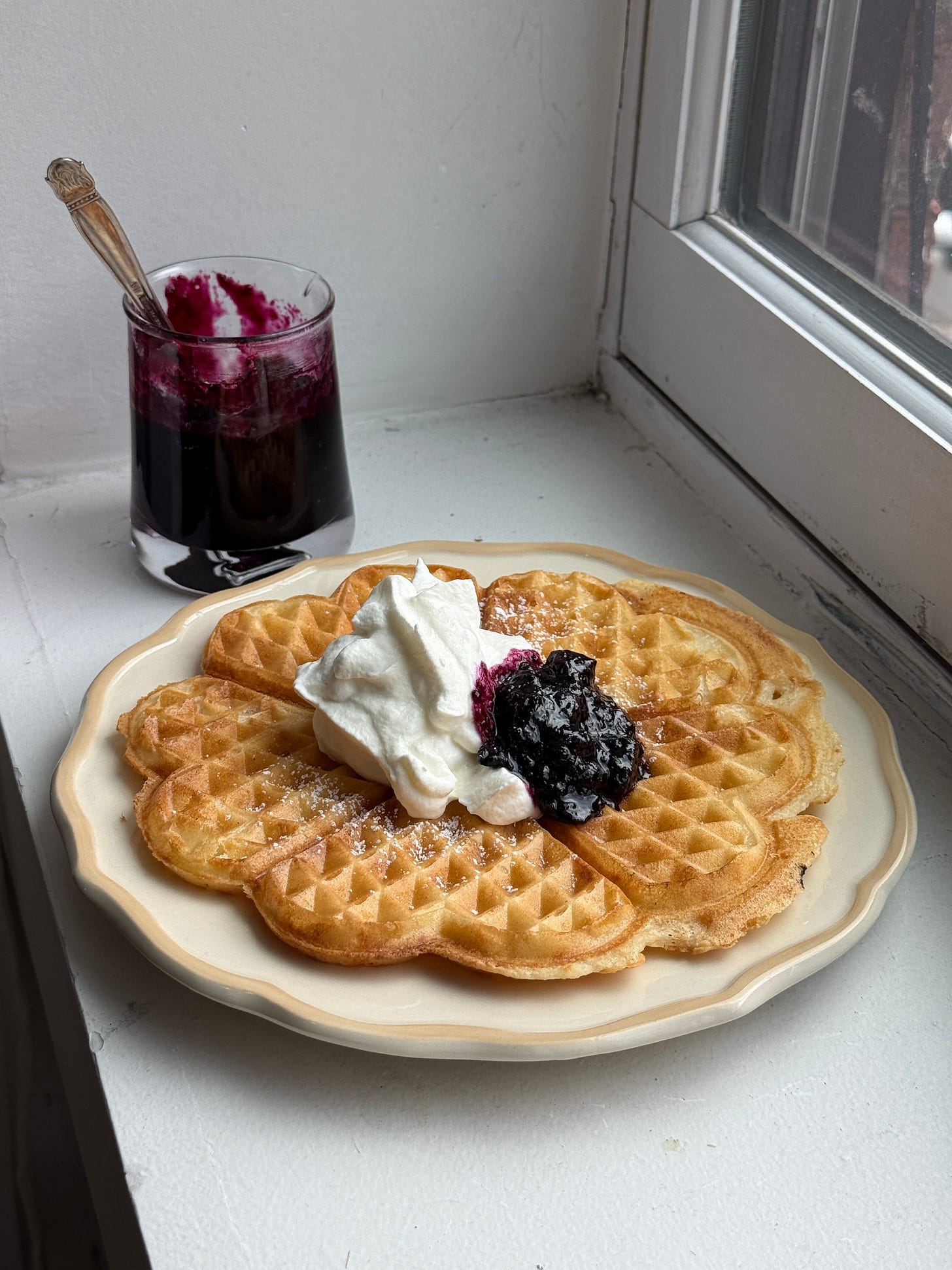 a plate with a swedish waffle topped with whipped cream and blueberry jam