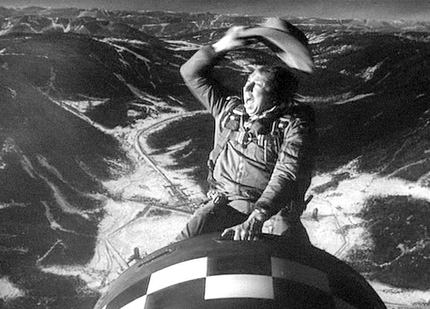 A crazed man riding a nuclear bomb like a rodeo while waving his hat and yeehawing