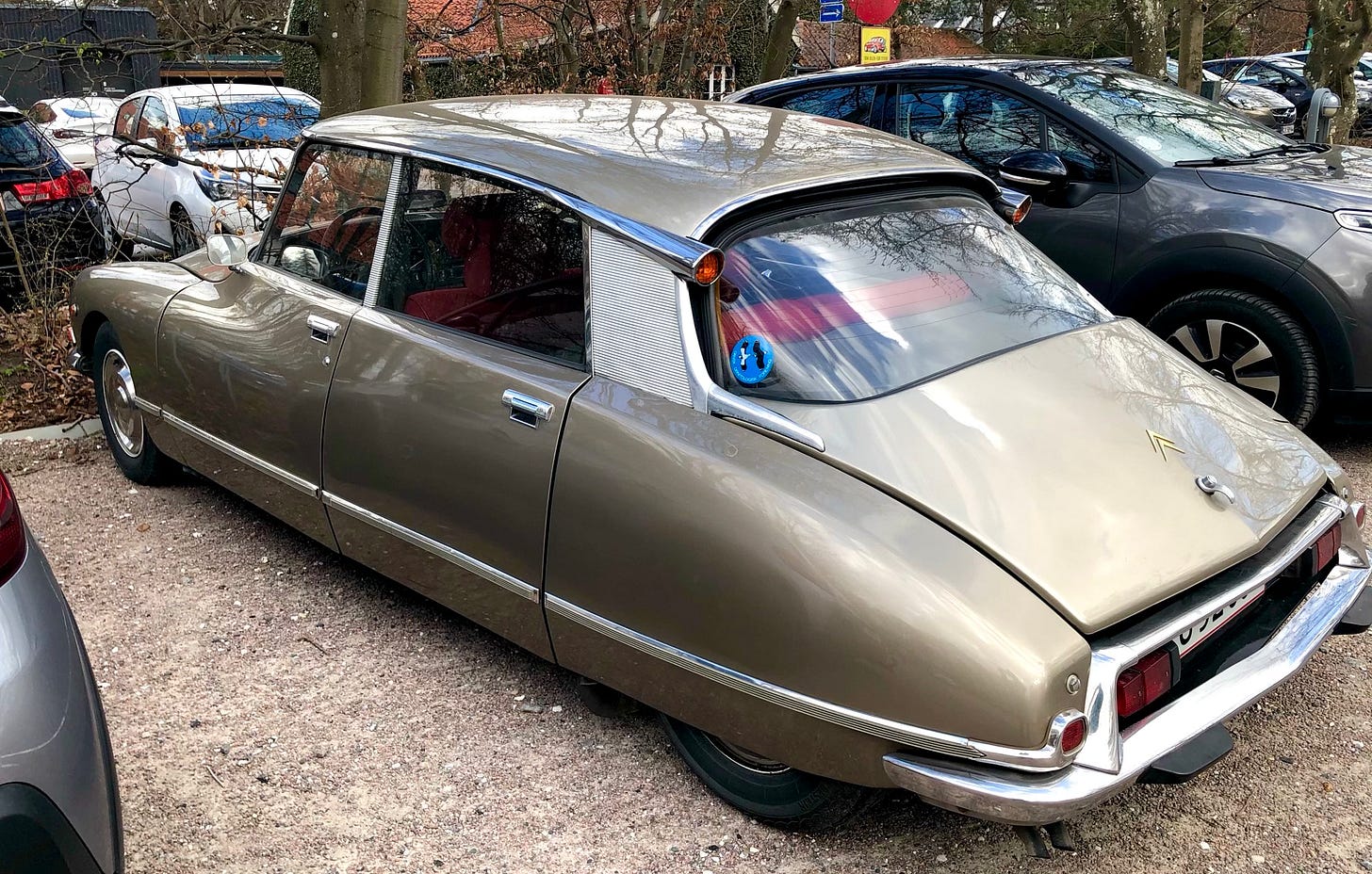 an old Citroen in a car park, wide bullet-shaped body, sunk down in parked position so rear wheels are barely visible