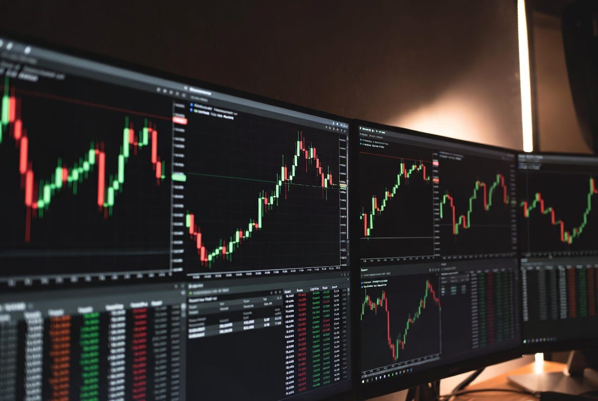 Multiple monitors displaying red and green cryptocurrency candlestick charts and order book data in a dark trading setup, representing active crypto market surveillance and analysis Multiple monitors displaying red and green cryptocurrency candlestick charts and order book data in a dark trading setup, representing active crypto market surveillance and analysis