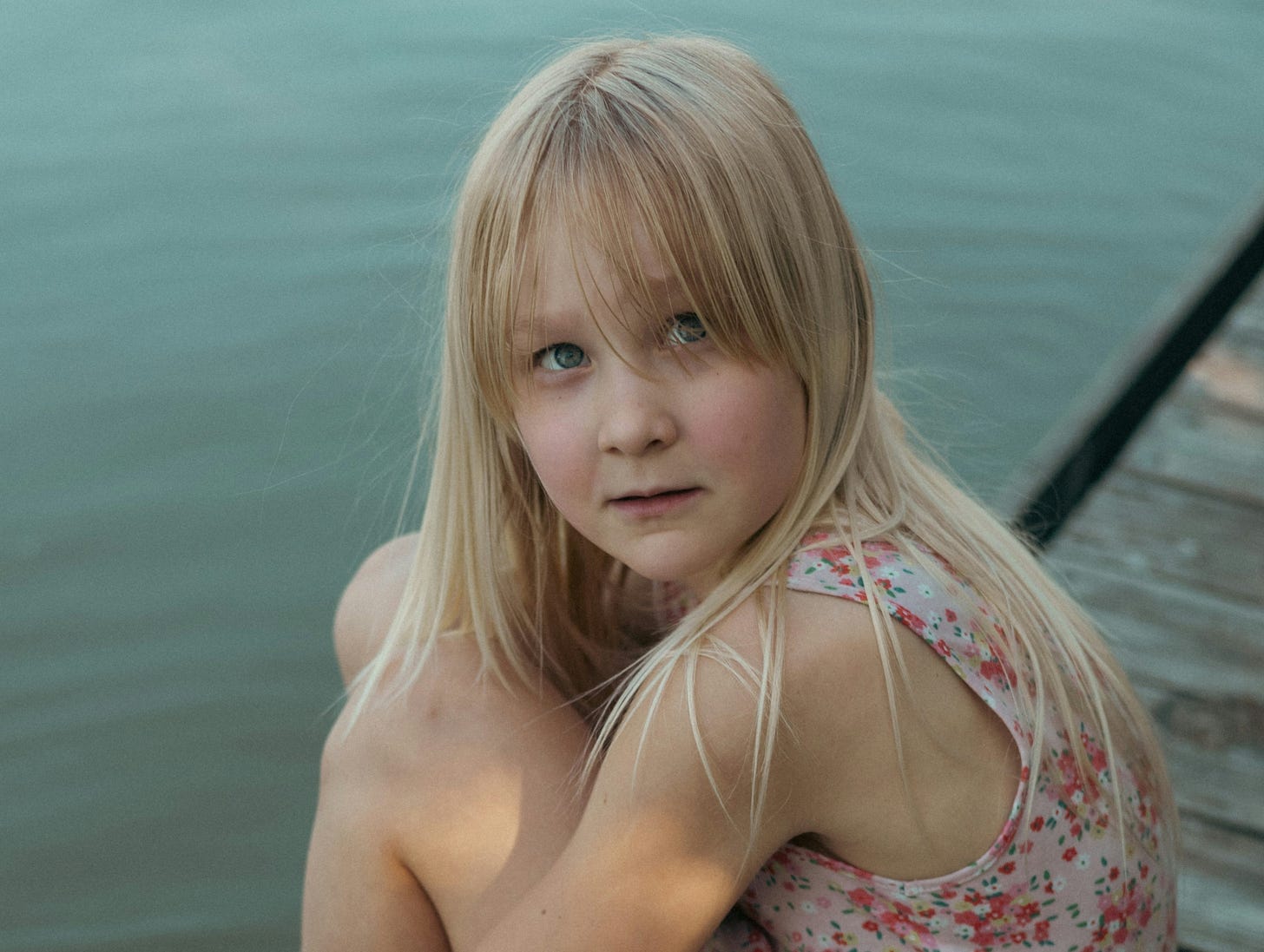 Girl sitting on wooden pier, looking at camera with a sad, thoughtful expression Girl sitting on wooden pier, looking at camera with a sad, thoughtful expression