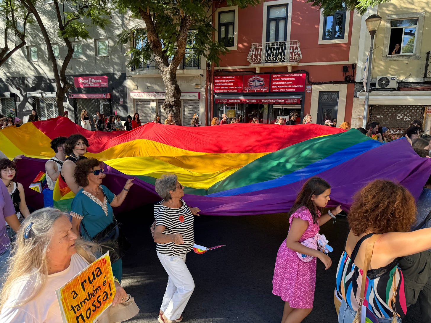 Marchers carry an enormous rainbow flag through a city street.