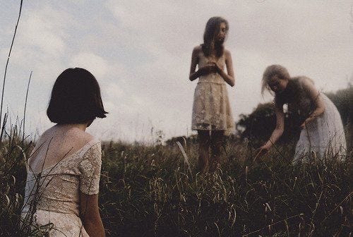 This may contain: three women are standing in tall grass and one is looking at the ground with her hands on her hips