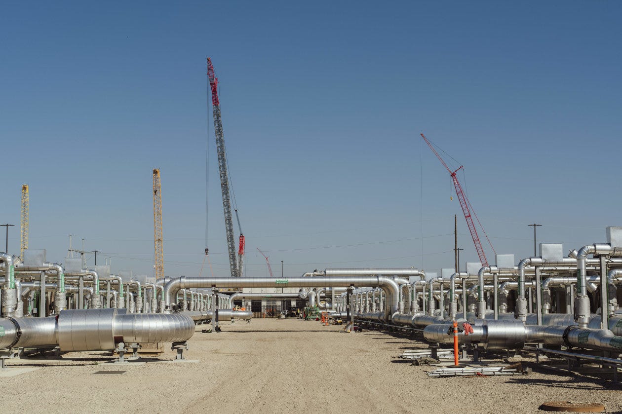 Construction site for a new data center with extensive cooling system pipes and several cranes under a clear sky.