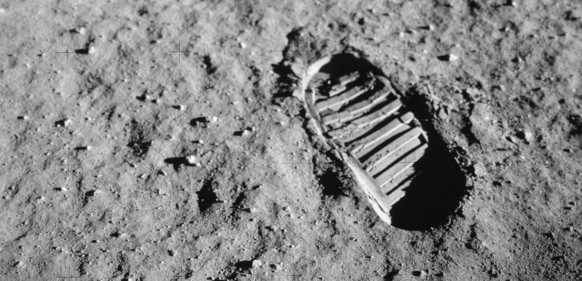 Close-up black-and-white photograph of a bootprint pressed into fine lunar soil on the moon’s surface during the Apollo 11 mission. The sharply detailed tread pattern contrasts against the soft, dusty terrain.