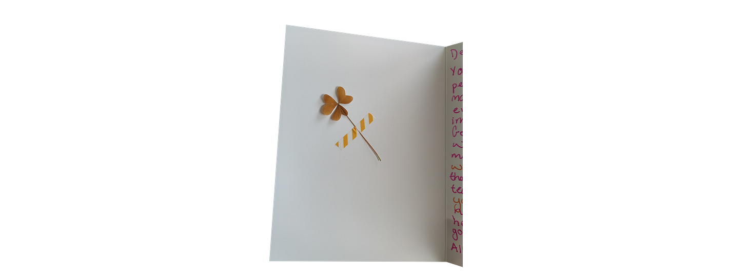 The inside of a card, with a dried clover taped on the left page.