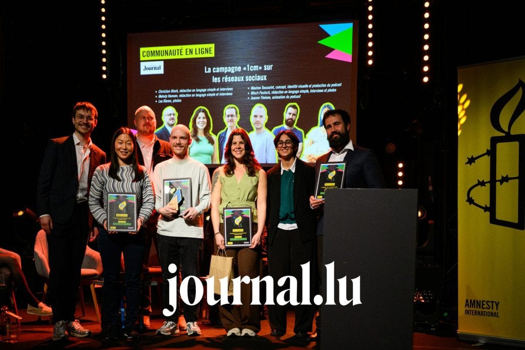 A group poses on a stage holding awards in front of a large screen about a social media campaign, with stage lights glowing and an Amnesty International banner at the side.