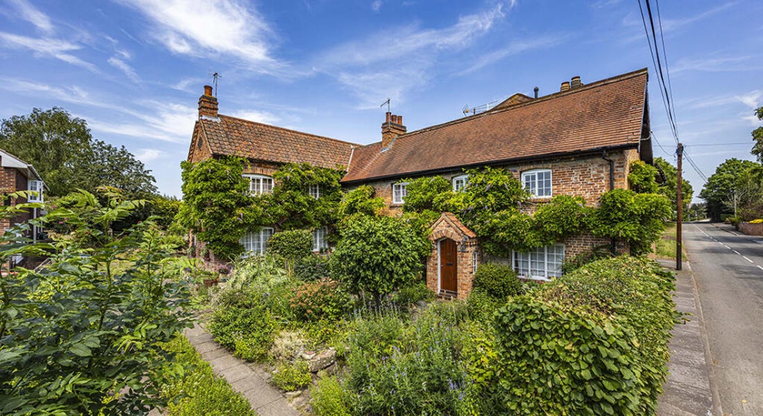 A brick house with a red door and greenery around it, with a road to the right A brick house with a red door and greenery around it, with a road to the right