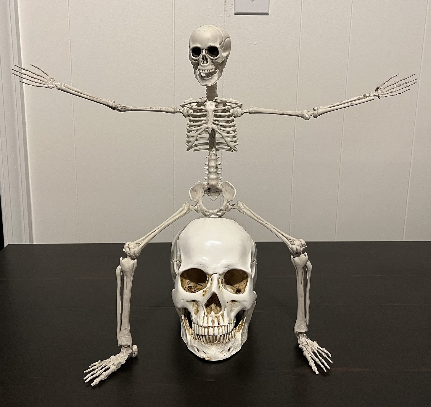 A toy skeleton sitting on top of a plastic skull.