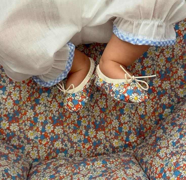 This may contain: a toddler's feet and shoes on a floral seat cushion with blue flowers