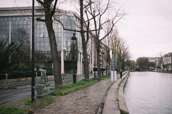 An urban canal with stone and paved paths, a few trees and glass buildings ahead.