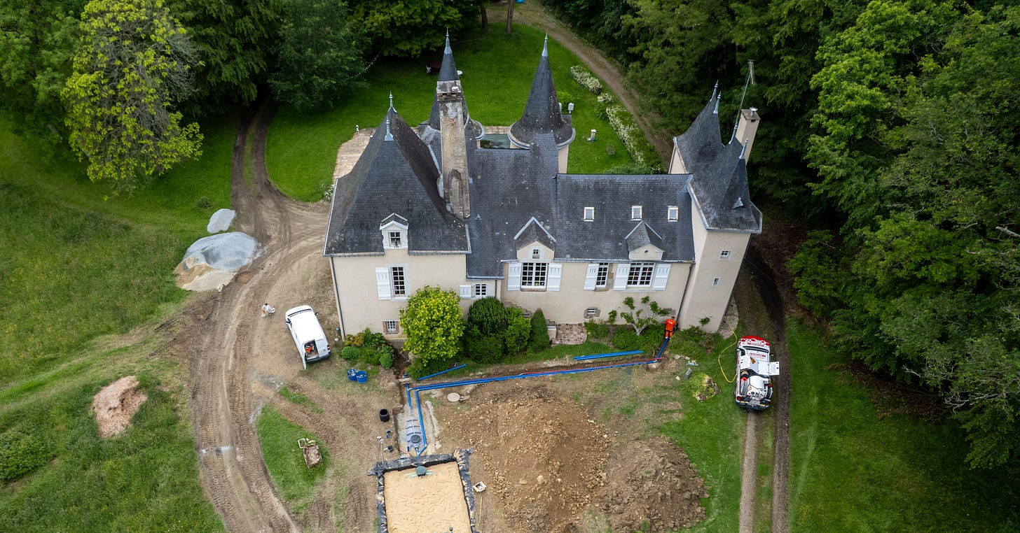 Aerial drone view of a French château during septic system installation, with excavated trenches, dirt mounds, the new tank, and workers visible in the foreground Aerial drone view of a French château during septic system installation, with excavated trenches, dirt mounds, the new tank, and workers visible in the foreground