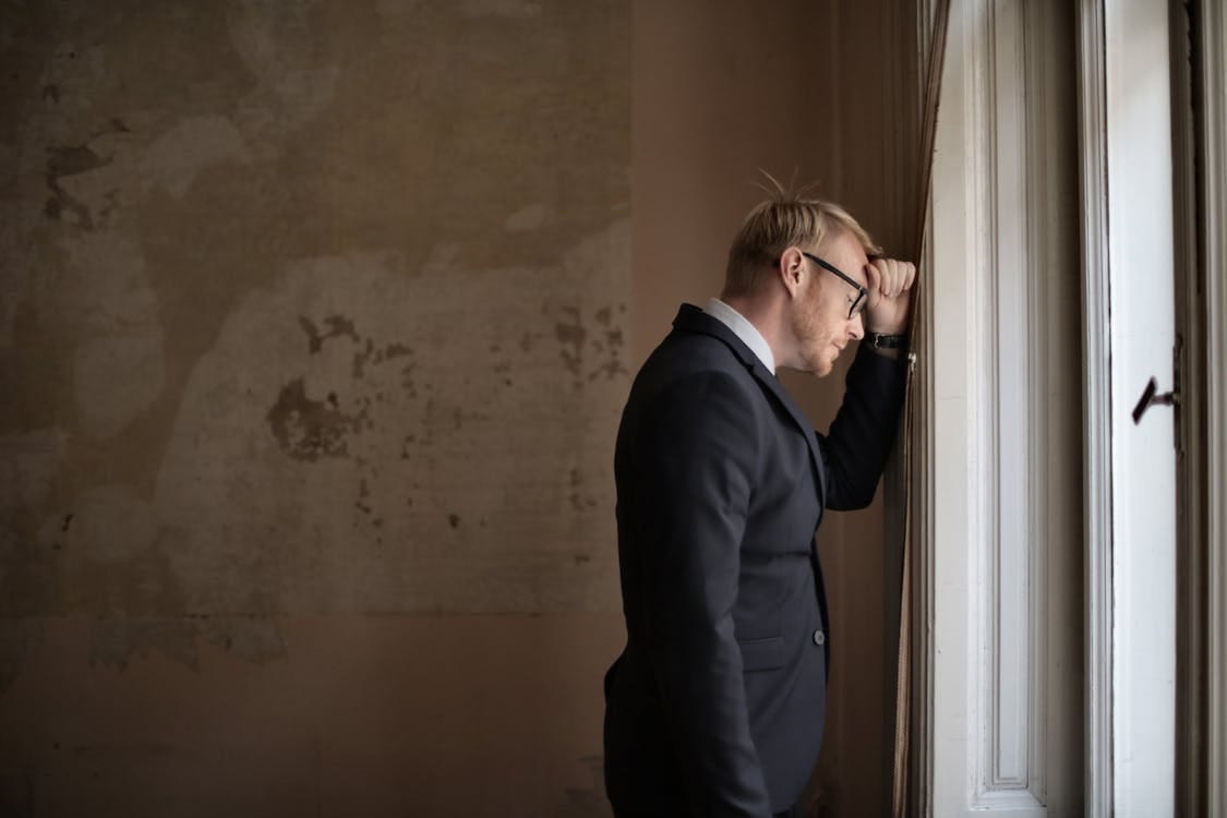 Free A worried businessman in a suit leaning against a window, expressing stress and concern. Stock Photo