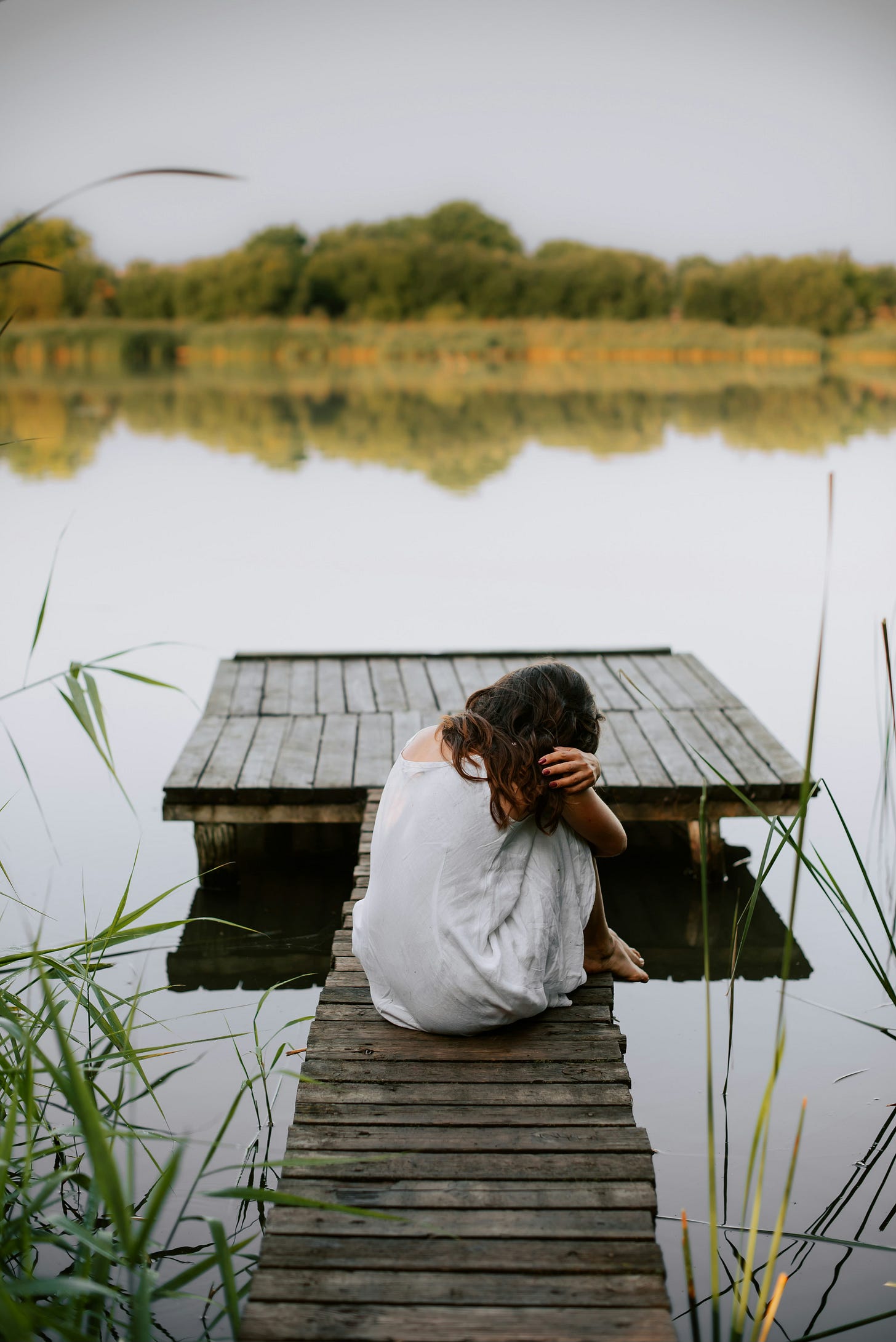 a girl hugging her knees by a lake