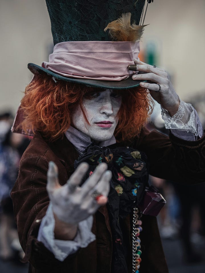 pictures of an enchanted forest, tones of orange and blue, and a man dressed as the Mad Hatter extending their hand to the observer in invitation.