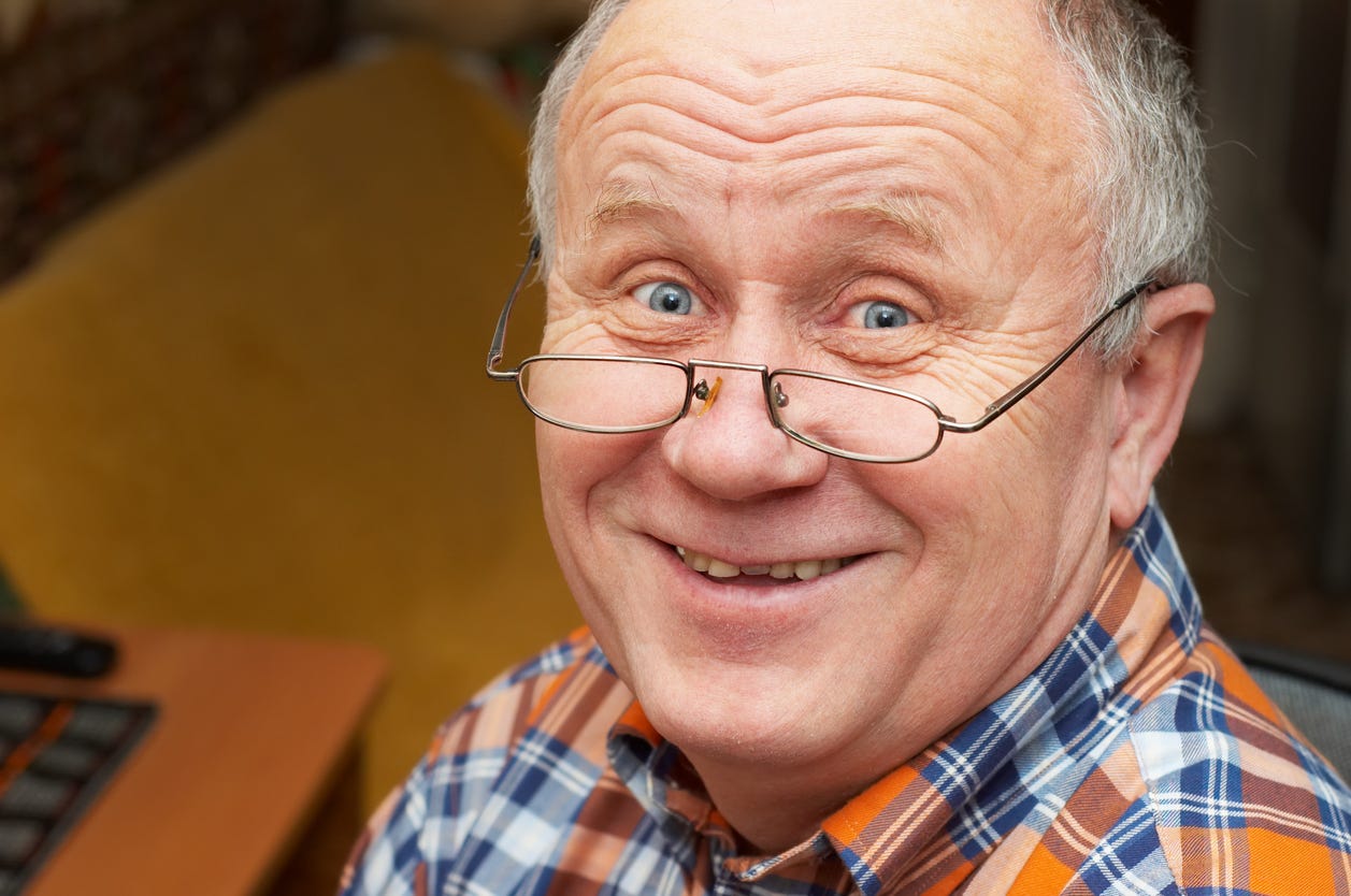 Tight headshot of smiling, bright-eyed white male with half eye glasses resting on his lower nose.