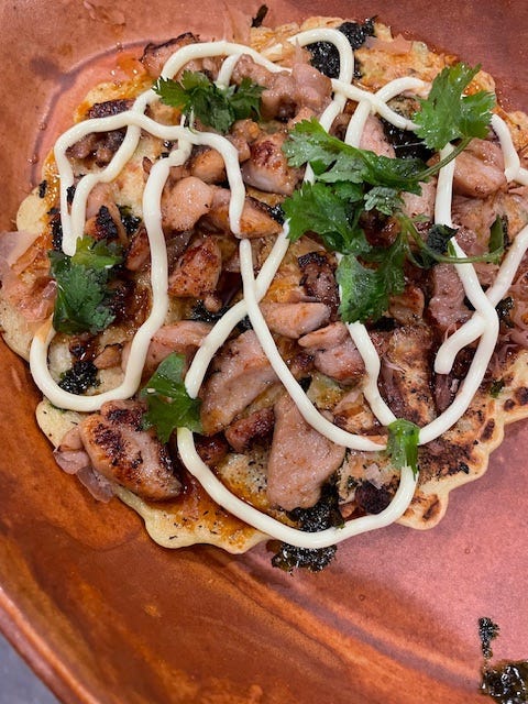 This giant pancake is topped with pieces of chicken and garnished with the sauces and cilantro.