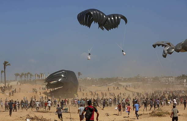 Palestinians gather to receive aid supplies dropped by military cargo planes using parachutes over Deir al-Balah, Gaza, on August 26, 2025. Efforts...
