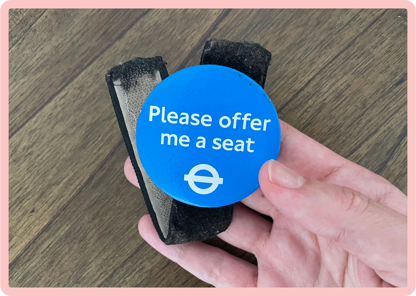 A close-up of a blue 'Please offer me a seat' badge which has been attached to a piece of black velvet, with velcro on one side, and is being held in a hand. A close-up of a blue 'Please offer me a seat' badge which has been attached to a piece of black velvet, with velcro on one side, and is being held in a hand.