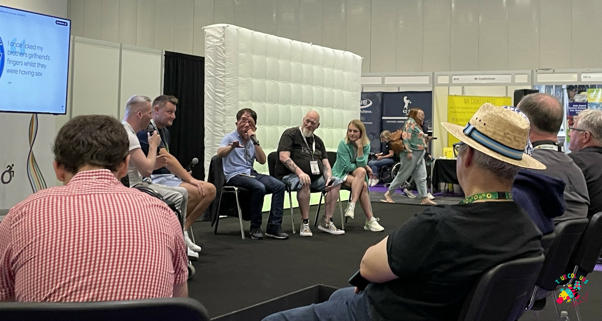 Photo shows an audience with the Grumpy Gits on stage.  There are 4 men and one woman.  All wearing trainers.  They look happy to be talking to each other.