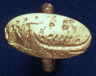 A gold ring with a large, flat oval bezel that has an image molded into it. The image is a scene with a woman and man standing on the shore on the left, with a boat approaching from the right. The boat is full of people, including one who is standing and holding a steering oar. Above the boat floats a tiny female figure and a tree.