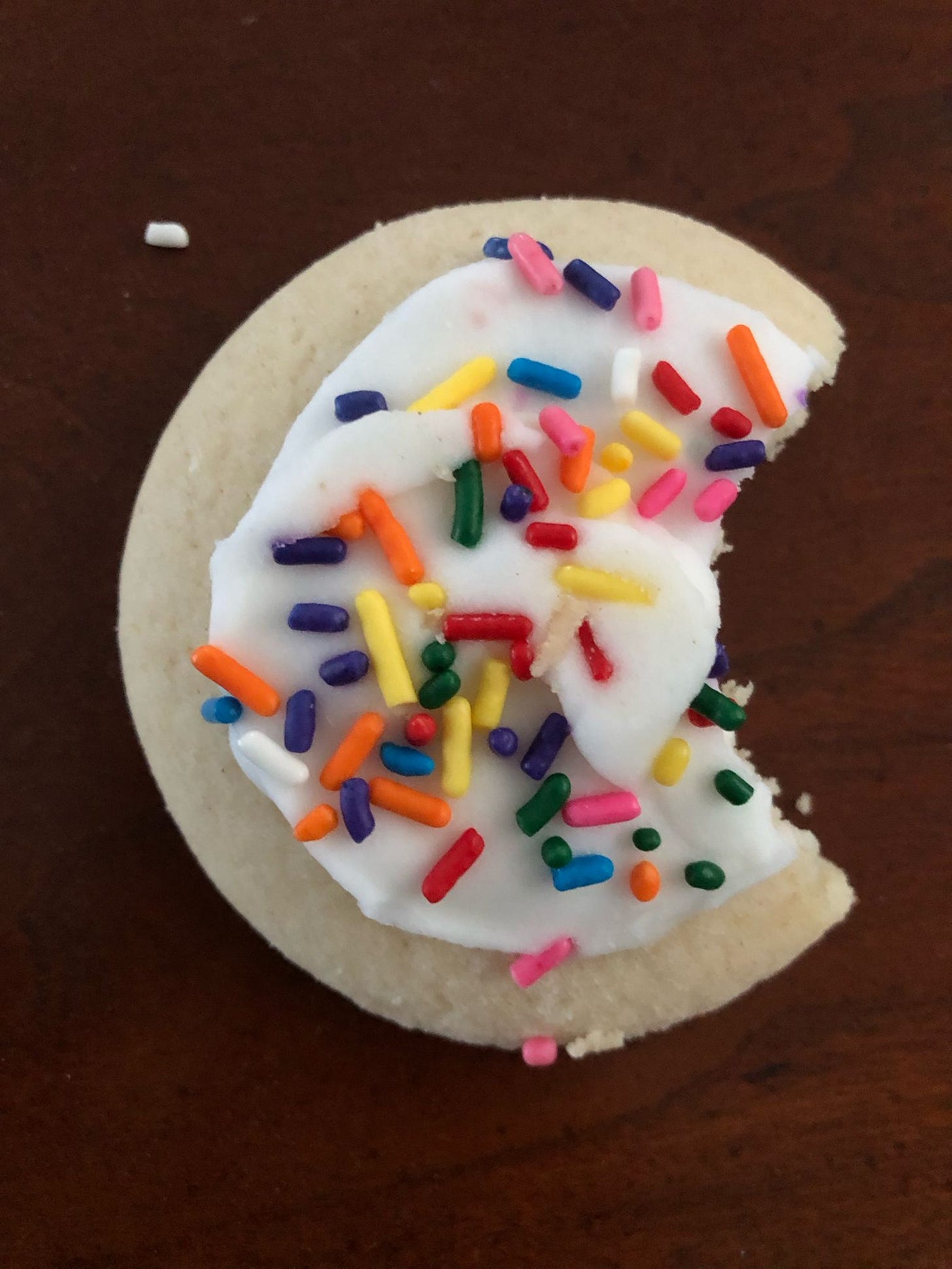 An iced sugar cookie with rainbow sprinkles; a bite has been taken