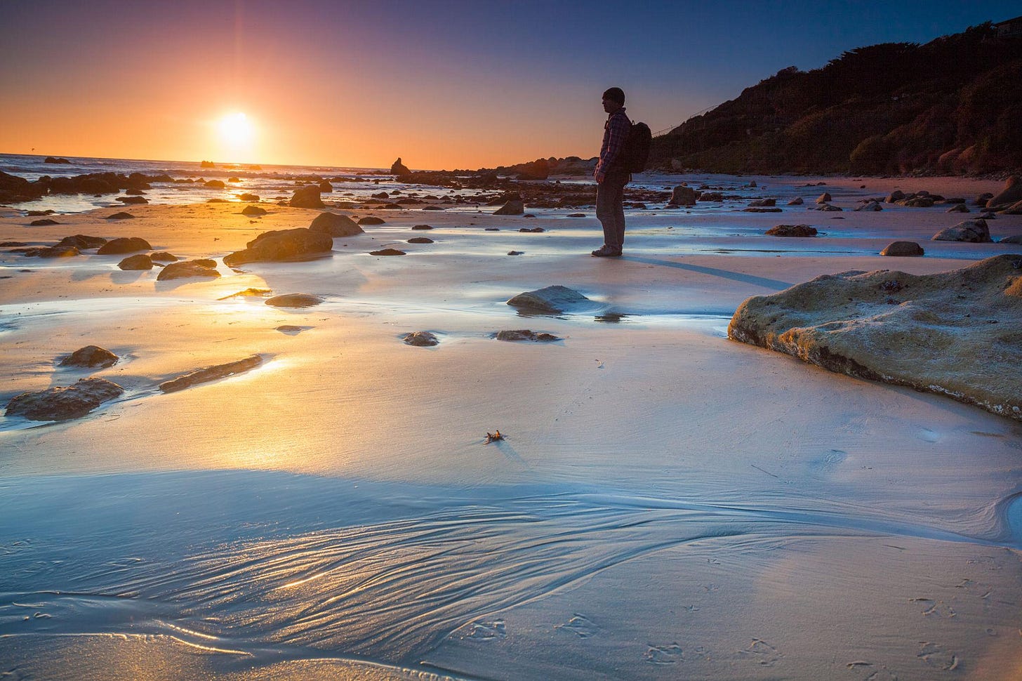 reflective silhouette at the shoreline at sunrise/sunset with a man watching the tide go out