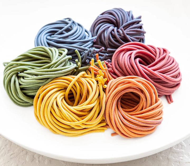Two photos of colorful pasta, one shaped like mini croissants and one with five round bunches of rainbow-colored bucatini