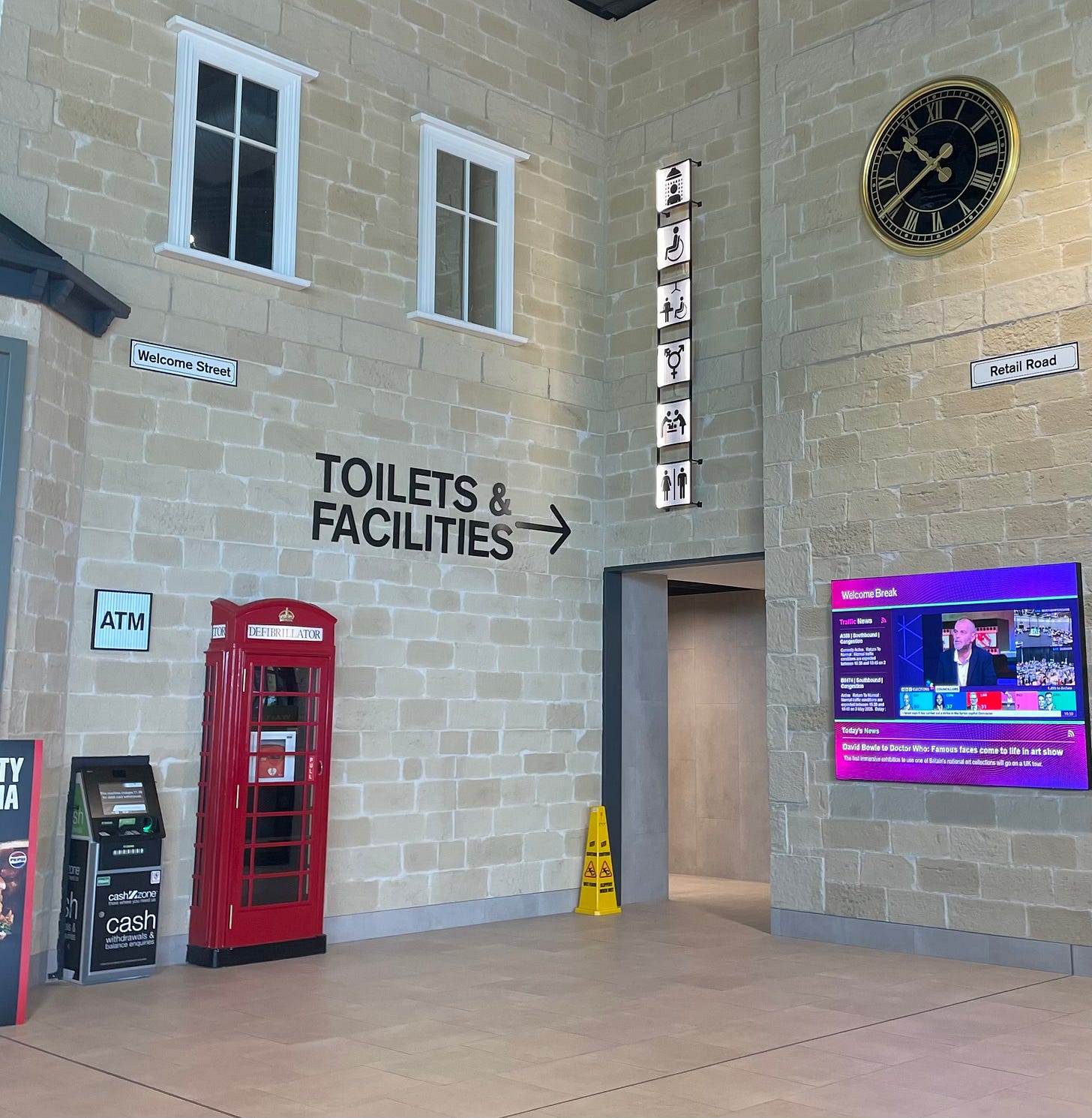 Inside Rotherham services. A 'stone' wall with a red telephone box and windows, which is actually the 'street' leading to the 'toilets and facilities'