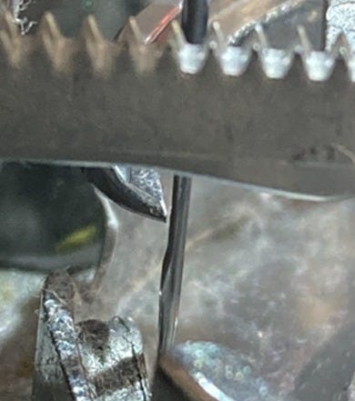 Close-up of a sewing machine hook point passing just behind the needle