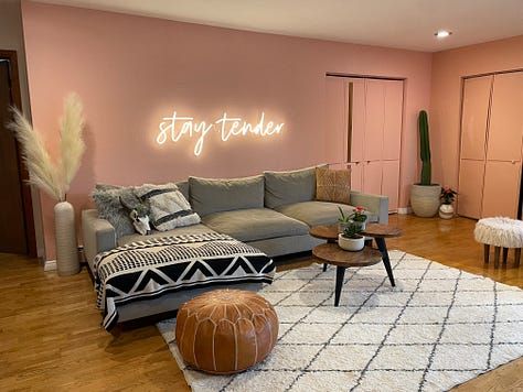 each photo is of Andrea and Meg's living room, painted in progressively different colors with slight alterations on decor at well. In first photo, wall is charcoal colored. Subsequently, emerald, light pink, wallpapered, white with a "stay tender sign", then white with a triptych of cacti.