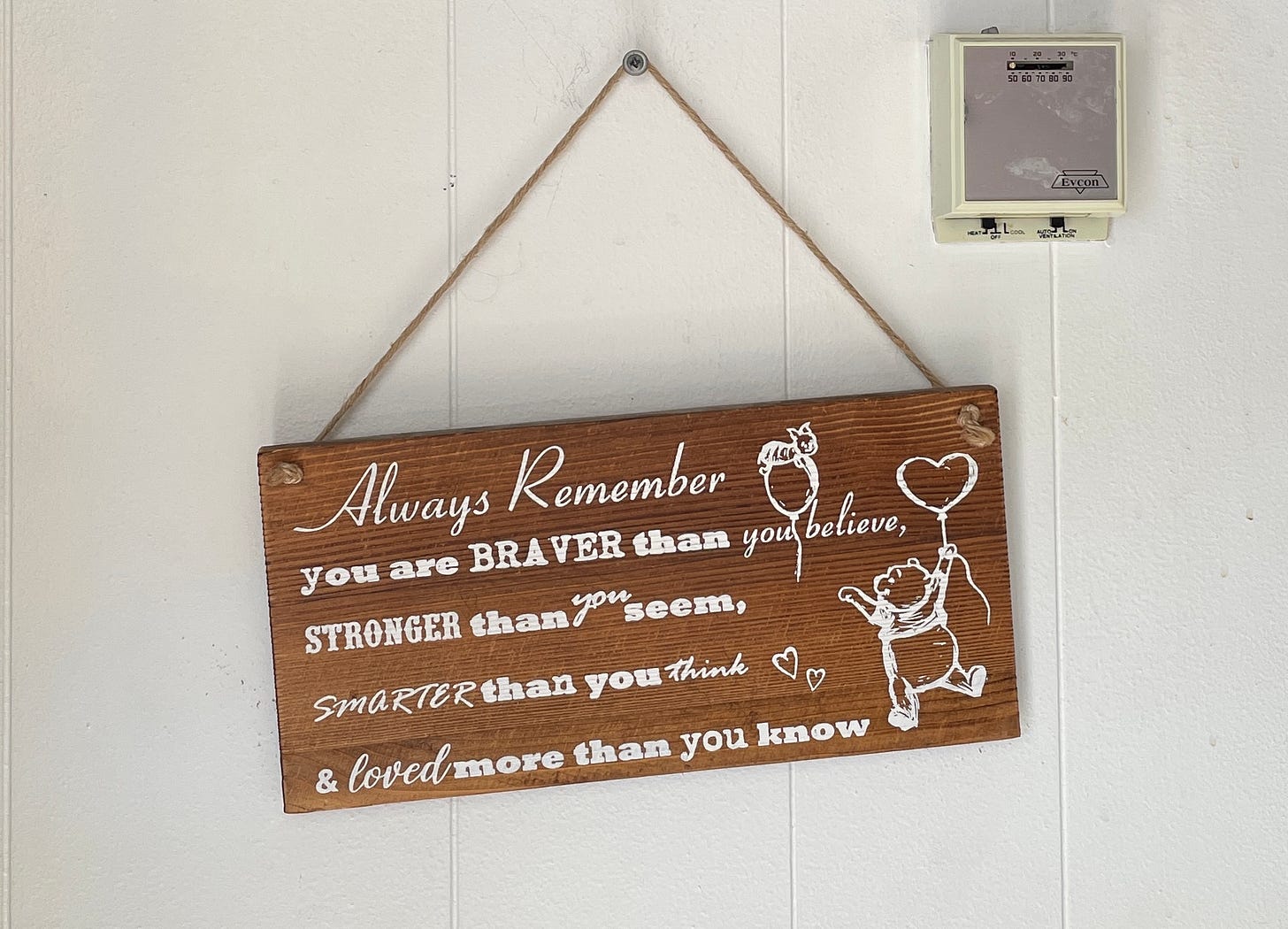 A wooden plaque hangs on the wall. It says "Always remember you are braver than you believe, stronger than you seem, smarter than you think & loved more than you know." It also features a drawing of Winnie-the-Pooh and hearts A wooden plaque hangs on the wall. It says "Always remember you are braver than you believe, stronger than you seem, smarter than you think & loved more than you know." It also features a drawing of Winnie-the-Pooh and hearts