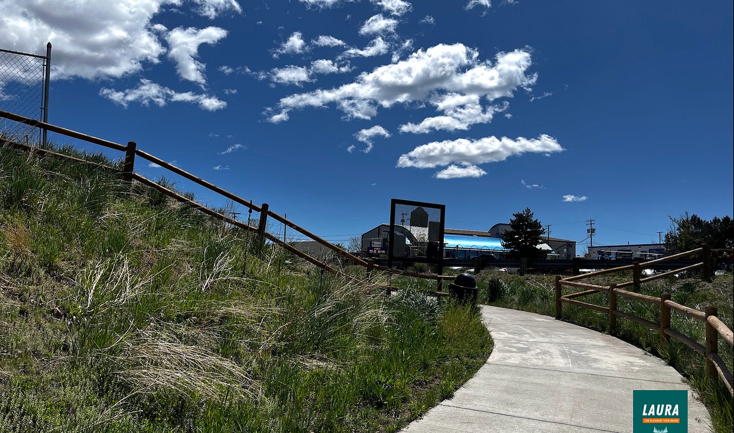 A concrete path curves uphill around a blind turn between a split rail fence A concrete path curves uphill around a blind turn between a split rail fence