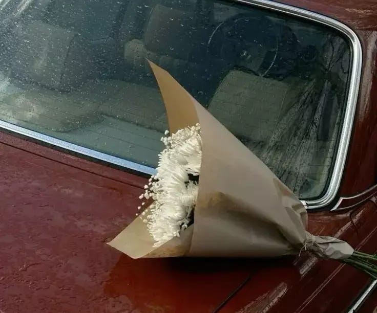 This may contain: a bouquet of flowers is placed on the hood of a red car in front of a window