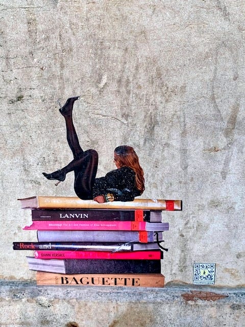 Street art of a woman lying back on a stack of books. She has one leg bent at the knee and the other leg in the air.