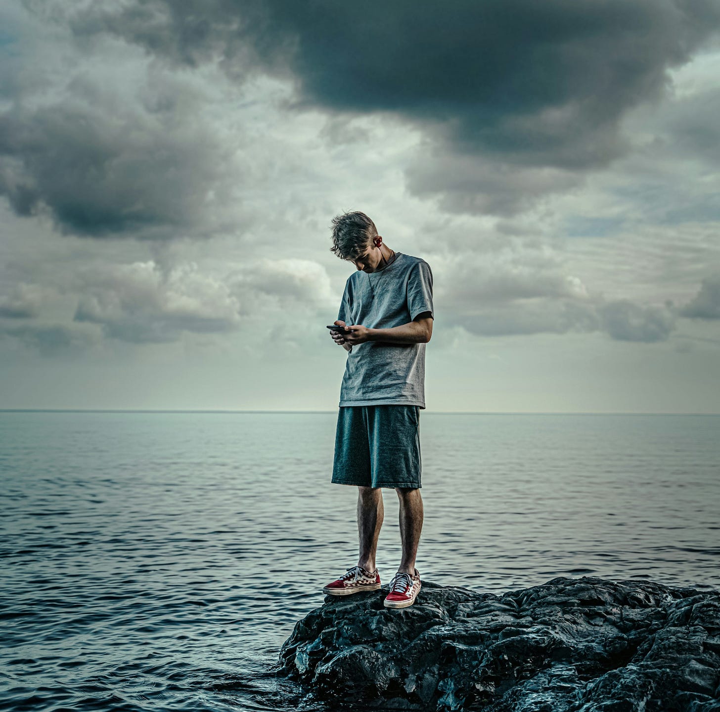 woman in white long sleeve shirt and blue skirt standing on rock in front of sea