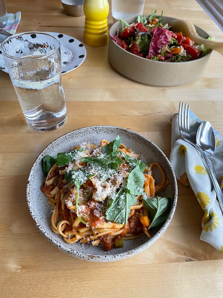 Dutch oven filled with lentil bolognese on the stove. A bowl of lentil bolognese with spaghetti topped with basil and parmesan on a dinner table.
