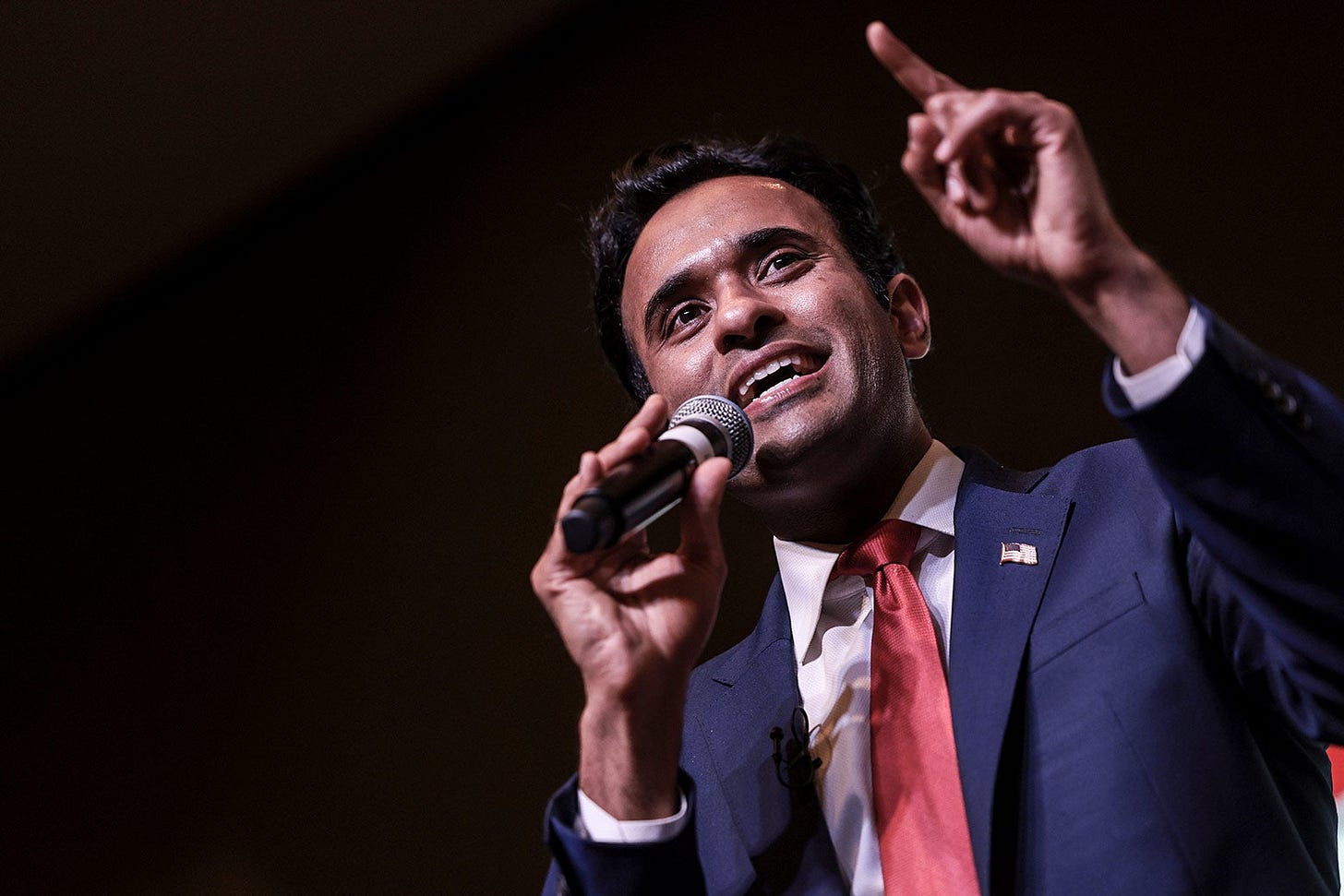 Vivek Ramaswamy holds a microphone and waves one finger in the air.