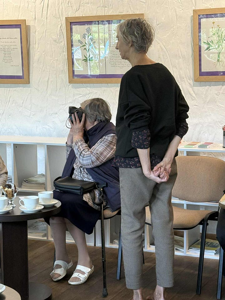 There are three images on the top, and two below. 1.	Activity workshop space inspired by the library’s natural environment and history. Photo by A. Petreike The environment was designed in reference to the library’s natural surroundings and historical background, reflecting the plant-themed concept of the workshop.  2.	Educational postcard with plant motif. Photo by A. Petreike Participant holding a plant-themed educational postcard, developed as part of the educational materials. The postcards invited participants to recognize familiar plants, color them and take them home to take home as a meaningful keepsake of the activity workshop. The back of the postcard featured the library contact person and their details, offering a way to connect.  3.	Educator interacting with participants. Photo by A. Petreike The educator engages participants by explaining and discussing different plants, fostering curiosity and sensory exploration (using a screen to show images, offering herbal tea to explore flavors, presenting postcards).  4.	Virtual reality experience. Photo by U. Padagiene Participant explores the library’s orangery using virtual reality glasses while the educator observes and guides the experience, enhancing engagement and sensory learning.  5.	Activity workshop session. Photo by A. Petreike